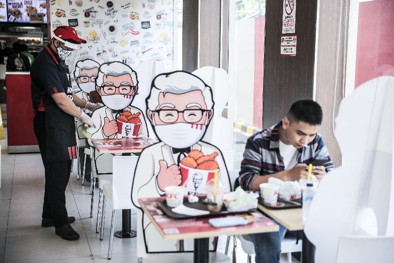 Visitors enjoy food at a table bounded by a banner with a character fast food restaurant Kentucky Fried Chicken, in Jakarta, Indonesia. (Photo by Jefta Images/Barcroft Media via Getty Images)